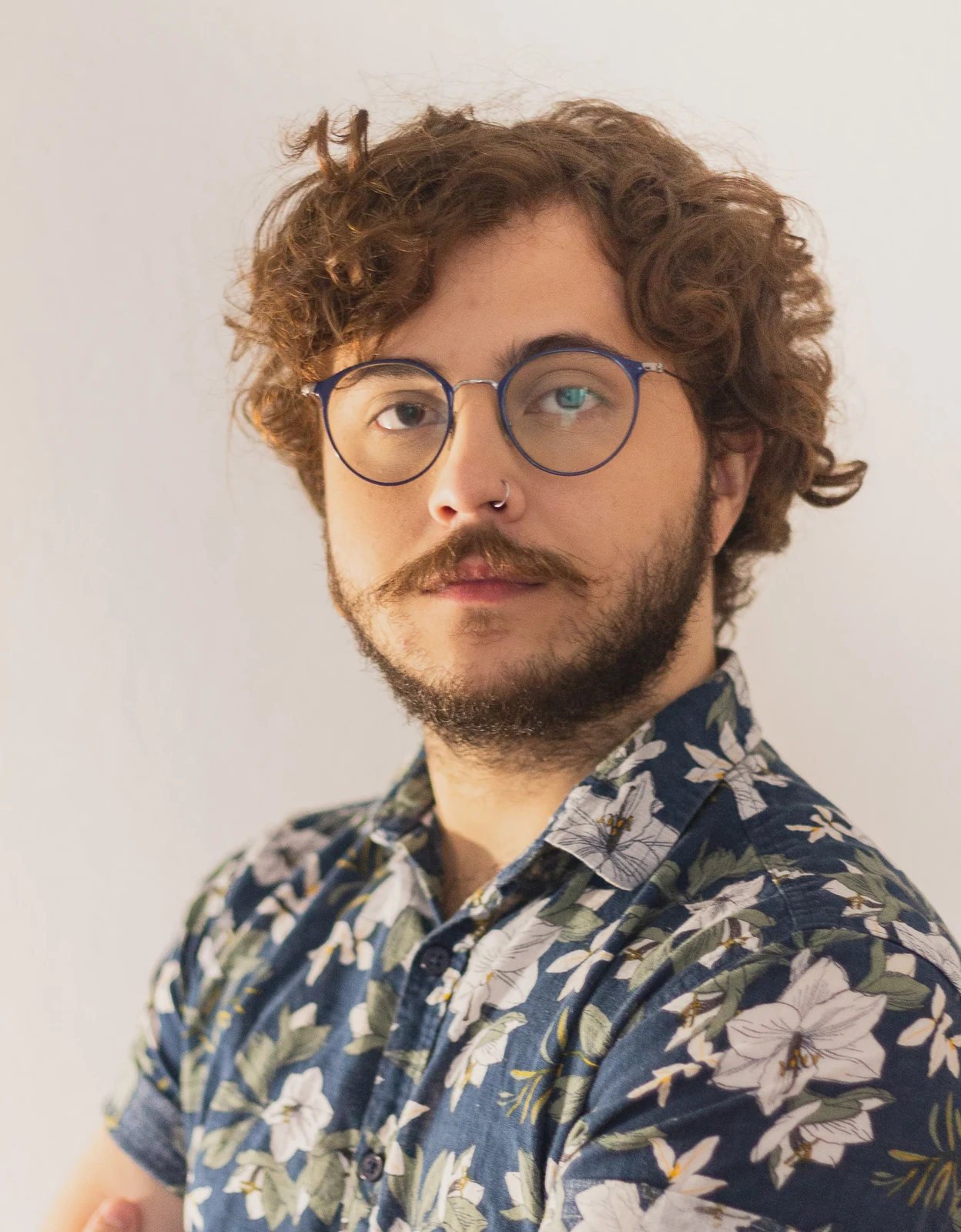 Retrato de Igor Rehem, de óculos e camisa estampada, contra uma parede clara